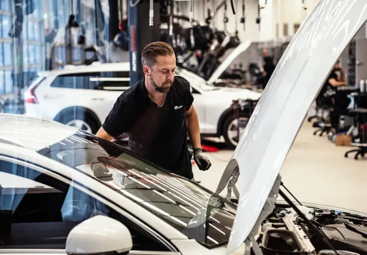 Mekaniker inspekterar en bil med öppen motorhuv. Frågan "hur lång tid tar en bilservice" kan besvaras snabbt med professionell hjälp.