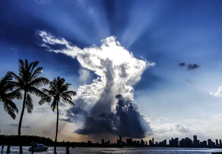 Dramatische Wolkenformationen im Himmel, die an eine engelhafte Gestalt erinnern, über einer Stadtkulisse mit Palmen. Ein Zeichen des Christentums?