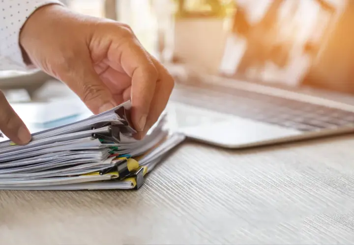 Dłoń przegląda stos dokumentów, szukając informacji, jak uzyskać odpis aktu urodzenia.