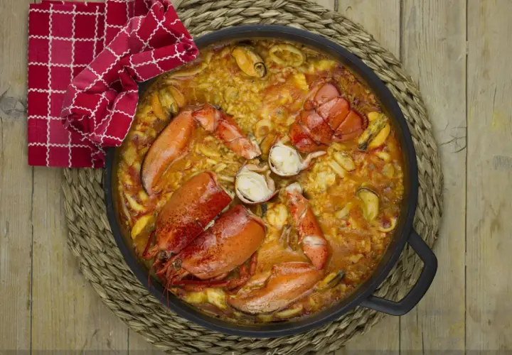 Paella de marisco con langosta, mejillones y calamares, servida en una paellera sobre una esterilla de mimbre.