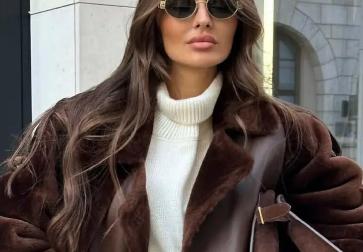 Elegancka kobieta w brązowym, futrzanym korzuszek i białym golfie, nosząca okulary przeciwsłoneczne.
