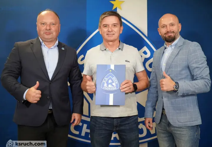 Trzech mężczyzn pozuje do zdjęcia z dokumentem K.S. Ruch Chorzów. Jeden z nich, nowy trener ruchu chorzów, trzyma dokument.