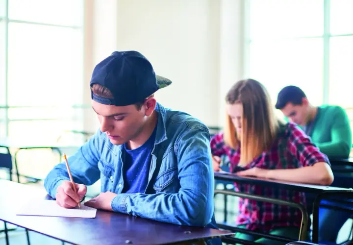 Ragazzo con cappellino scrive concentrato durante un esame. Il suo **did inglese** è importante per il futuro.