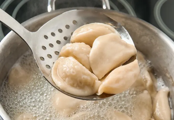 Gorące pierogi z serem, gotowane według przepisu babci, wyjmowane łyżką cedzakową z bulgoczącego garnka.