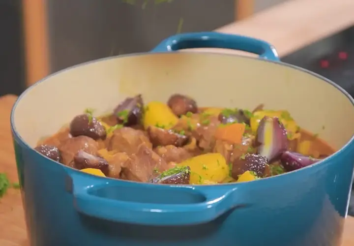 Un plat mijoté de navarin d'agneau, avec des morceaux de viande tendres, des carottes, des oignons rouges et des pommes de terre, garni de persil frais.
