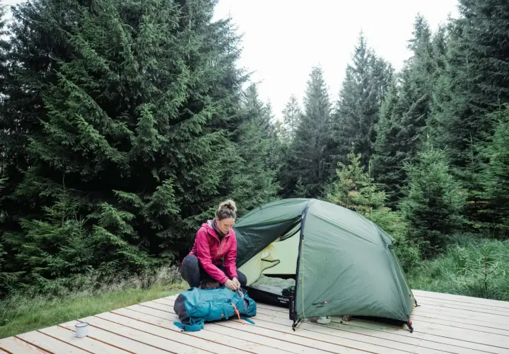 Une femme prépare son sac à dos près d'une tente dans une forêt de sapins. Une scène de camping en Allemagne.