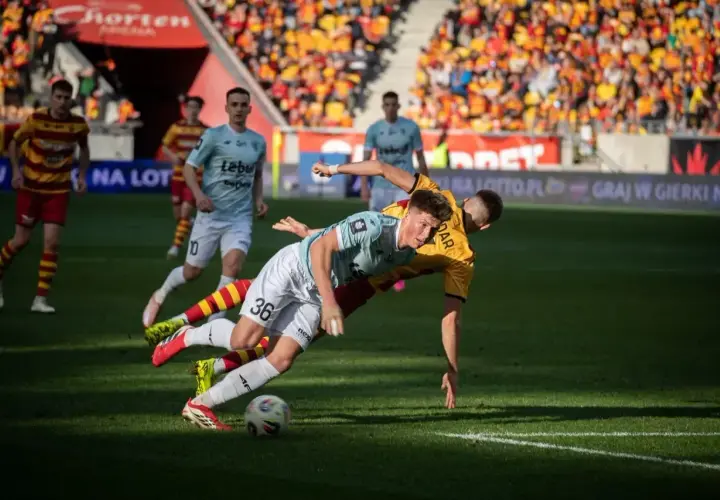 Zacięta walka o piłkę podczas meczu Jagiellonia Białystok – Piast Gliwice. Dwóch zawodników walczy o panowanie nad futbolówką na murawie.