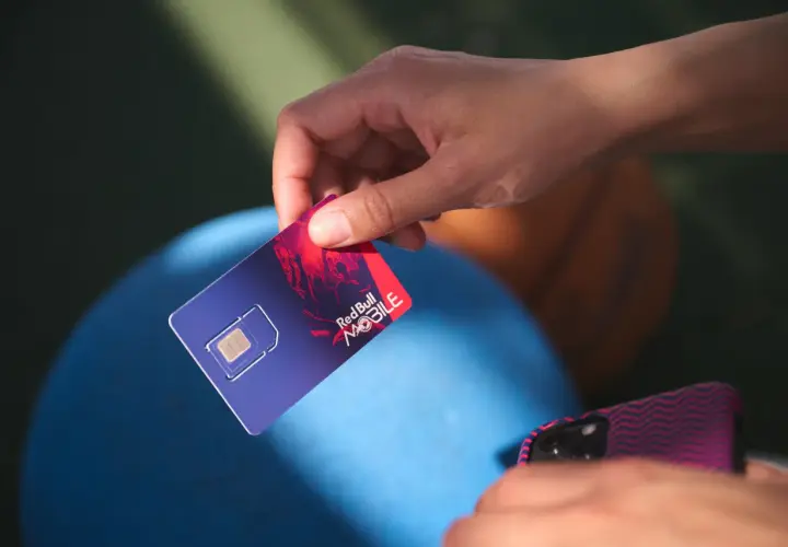 Dłoń trzyma kartę SIM Red Bull MOBILE, gotową do podróży po Europie. Internet na wyciągnięcie ręki!