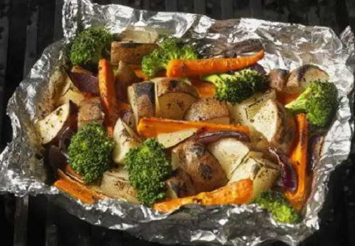 Légumes variés (pommes de terre, carottes, brocolis, oignons rouges) cuits en papillote sur un barbecue, prêts à être dégustés.
