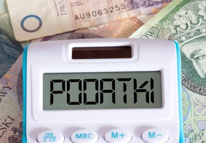 Kalkulator z napisem "PODATKI" na tle polskich banknotów. Czas na rozliczenie PIT 28 druk.