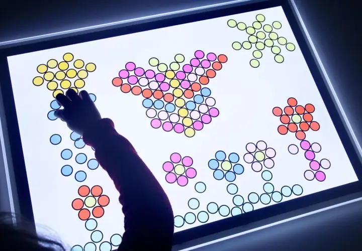 Niño/a creando figuras con piezas de colores sobre una mesa de luz, fomentando sus actividades creativas.