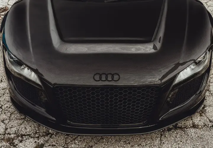 Przód czarnego auta sportowego z maską z włókna węglowego. Widać reflektory, grill i logo Audi.