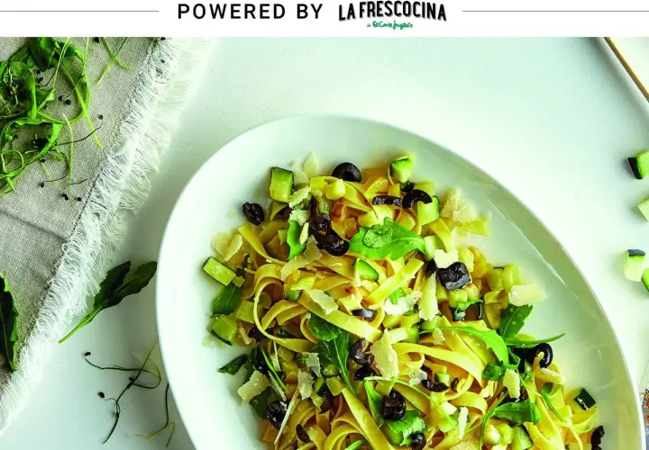 Pasta con verduras frescas, aceitunas negras y queso rallado, servida en un plato blanco.