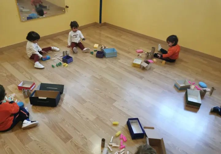 Niños pequeños exploran materiales diversos, cajas y pinzas, aprendiendo sobre el juego heurístico.