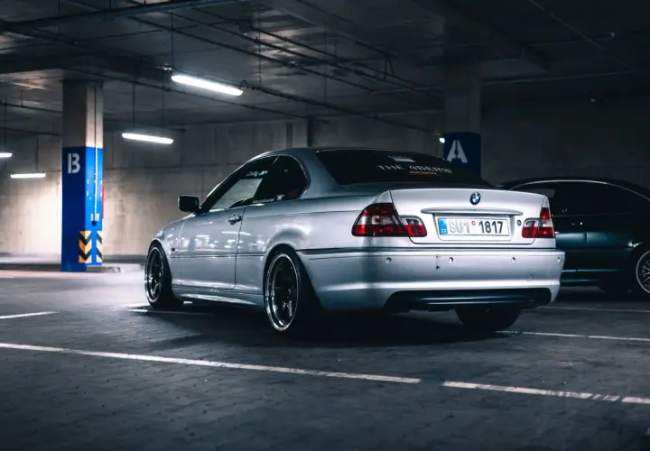 Srebrne BMW serii 3 (m54) z przyciemnianymi szybami i czarnymi felgami stoi na parkingu podziemnym.
