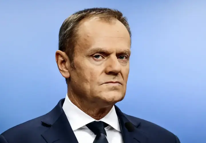 Portret Donalda Tuska w granatowym garniturze i białej koszuli na jasnoniebieskim tle.