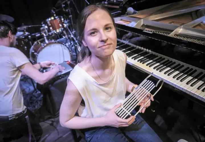 Kobieta z instrumentem muzycznym przed fortepianem i perkusją.