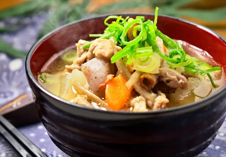 A steaming bowl of tonjiru recipe, filled with pork, vegetables, and topped with fresh green onions.
