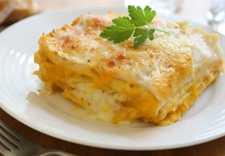 Une part de lasagne de butternut dorée et gratinée, garnie d'une feuille de persil, sur une assiette blanche.
