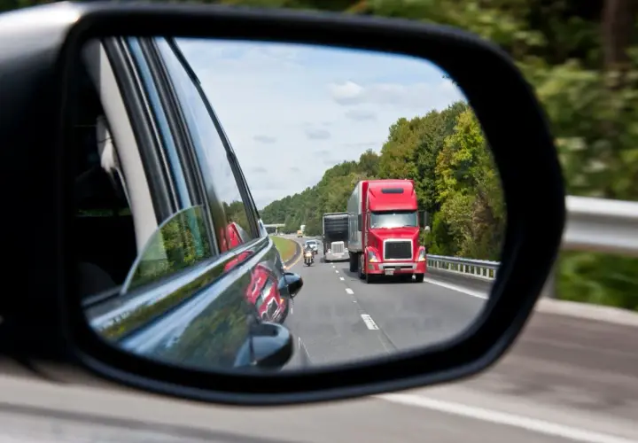 Reflejo en el espejo retrovisor: un camión rojo y una moto circulan por la carretera. ¡Atención! una moto puede adelantar por la derecha.