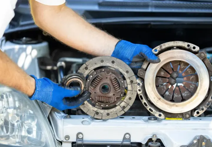Mechanik w niebieskich rękawiczkach pokazuje zużyte części sprzęgła. Poznaj wymiana sprzęgła koszt i dowiedz się, kiedy warto je wymienić.