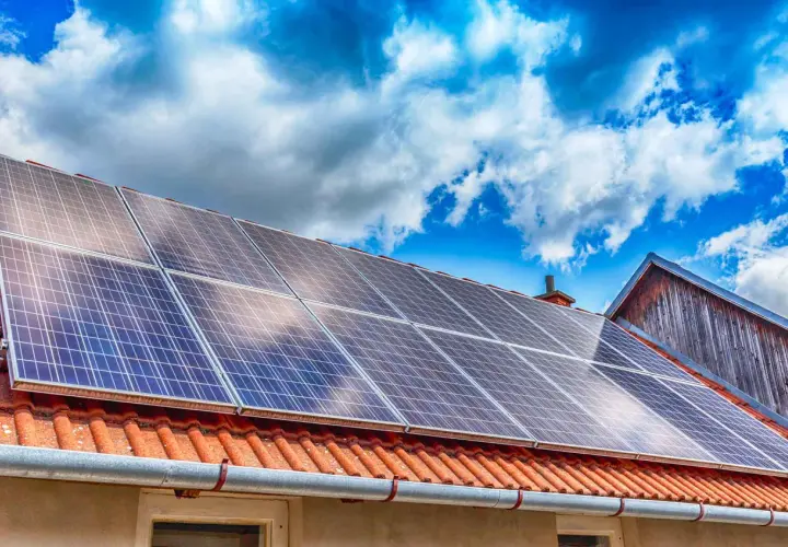 Panneaux solaires sur un toit de tuiles rouges, sous un ciel bleu et nuageux. Une installation qui assure une garantie pour l'avenir.