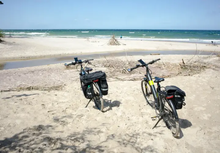 Dwa rowery z sakwami na piaszczystej plaży, gotowe na odkrywanie tras rowerowych nad morzem.