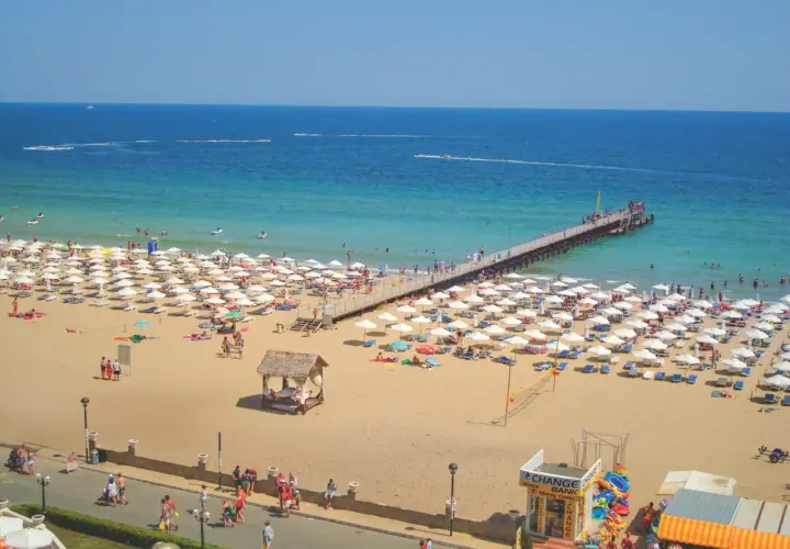 Słoneczny Brzeg, Bułgaria: plaża pełna białych parasoli, molo i turystów cieszących się słońcem i morzem.