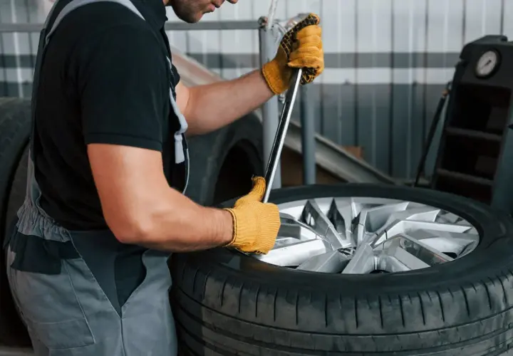 Mechanik w żółtych rękawiczkach używa klucza do opony, pokazując, jak ściągnąć oponę z felgi domowym sposobem.