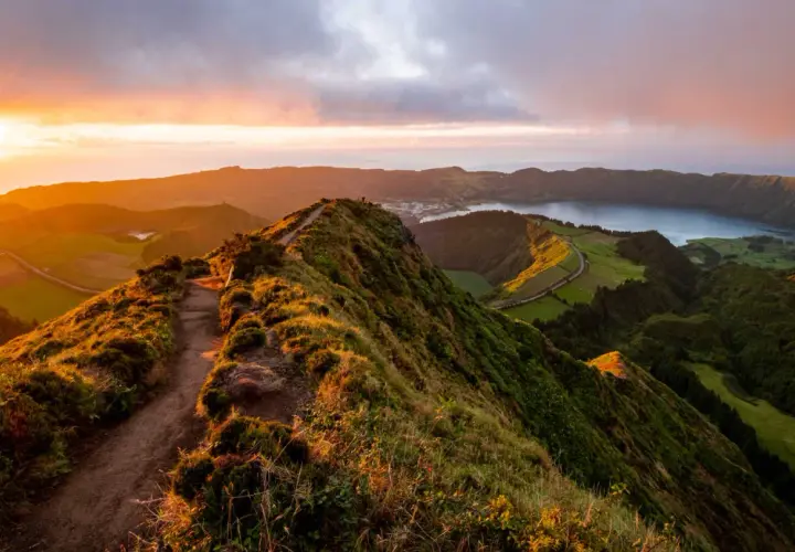 Magnifique paysage des Açores au coucher du soleil, avec un sentier serpentant sur une crête verdoyante menant à un lac paisible.