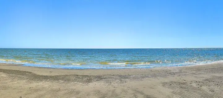 Vaste étendue de sable et de mer au Lido degli Estensi sous un ciel bleu clair. Des vagues douces caressent le rivage.