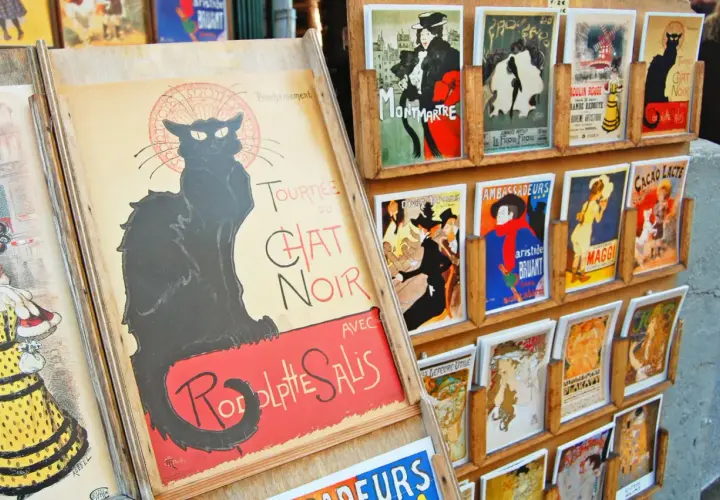 Affiches de chat art, dont une grande affiche du Chat Noir, exposées sur un présentoir en bois.