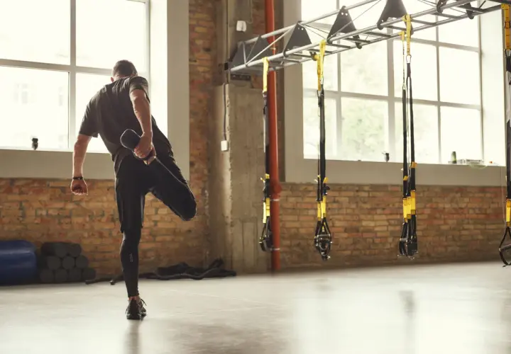 Hombre estirando la pierna, un ejemplo de la definición de calentamiento en un gimnasio con ladrillos y TRX.