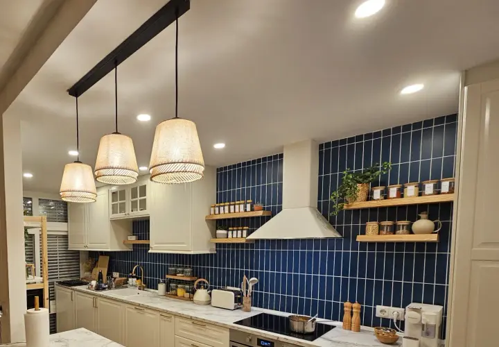 Una lámpara negra y madera ilumina esta cocina moderna con azulejos azules y encimeras de mármol.