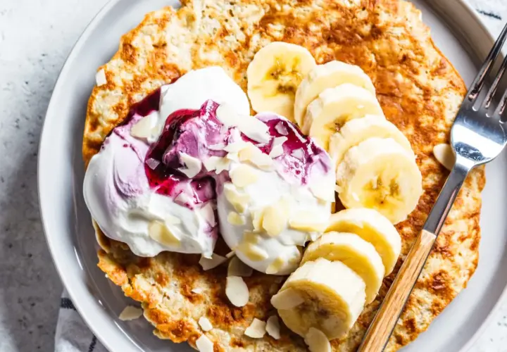 Puszysty omlet bananowy z jogurtem, musem jagodowym i płatkami migdałów na talerzu.