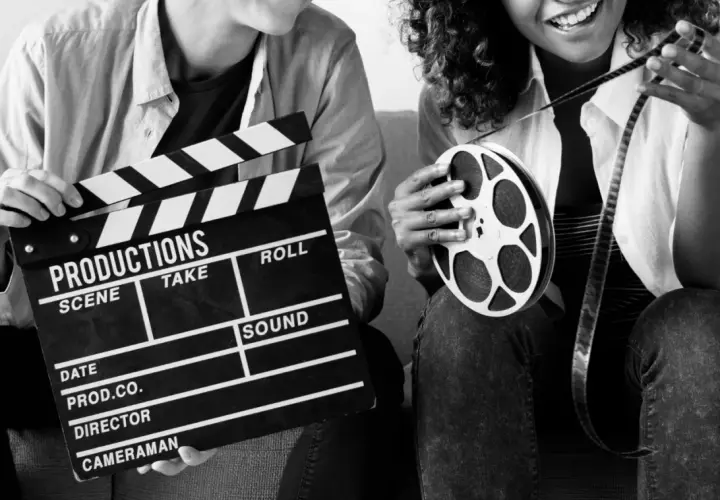 Dwie osoby z klapsem filmowym i rolką taśmy filmowej. Zastanawiasz się, ile zarabia reżyser filmowy?