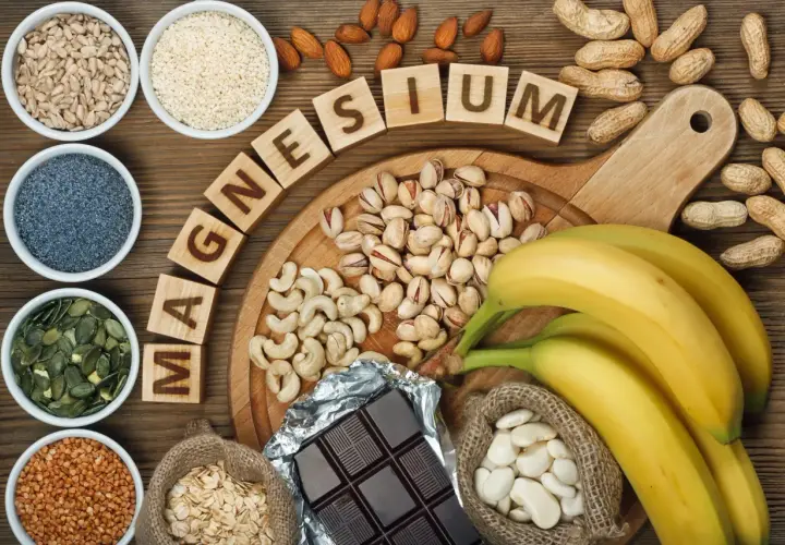Magnesium-reiche Lebensmittel wie Sesam, Nüsse, Bananen und dunkle Schokolade sind auf einem Holztisch arrangiert.