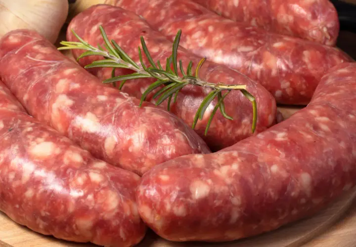 Surowe kiełbaski, czyli salsiccia, z gałązką rozmarynu i czosnkiem. Idealne do grillowania.