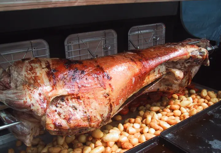 Gigot à la broche doré et juteux, rôti lentement avec des pommes de terre et des tomates cerises en dessous.