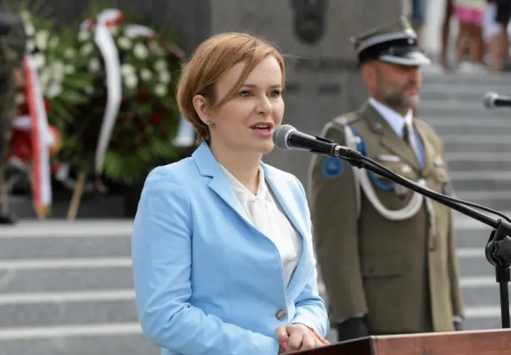 Anna Krupka w błękitnej marynarce przemawia przy mikrofonie. W tle żołnierze i wieńce. Ile milionów złotych oszczędności wykazała w oświadczeniu?