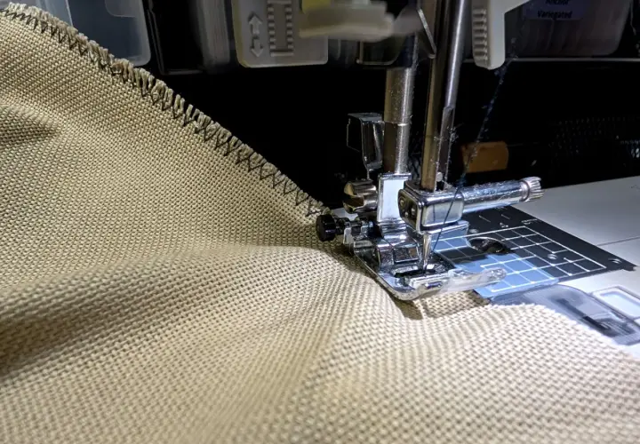 Sewing a zigzag stitch on a tan fabric to prevent fraying. This technique helps keep edges neat, unlike how some flannel might fray.