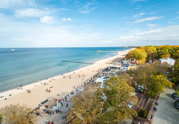 Słoneczny deptak w Kołobrzegu tętni życiem. Ludzie spacerują po plaży i promenadzie, ciesząc się jesiennym słońcem i widokiem na morze.