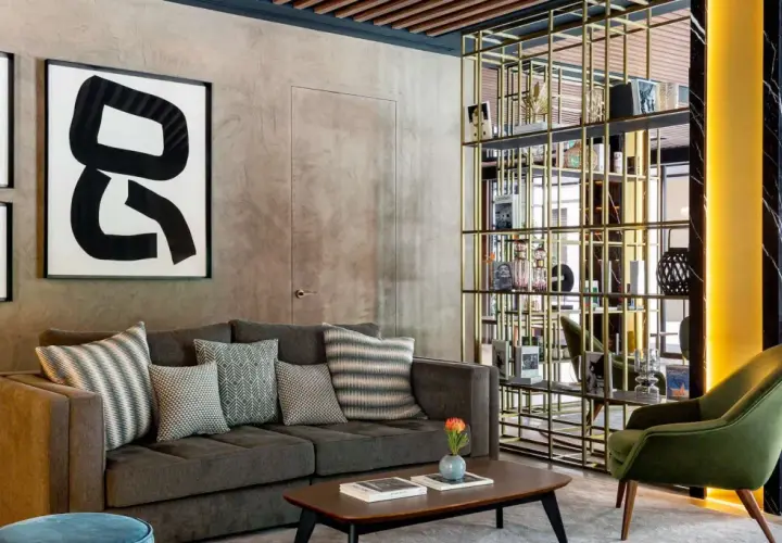 Sofá gris con cojines decorativos, mesa de centro y estantería dorada en un lobby de Radisson Collection.