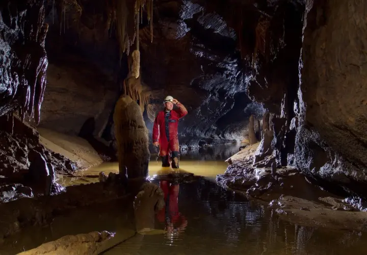 Eksplorator w jaskini, zanurzony po kolana w wodzie, odkrywa tajemnice speleologii.