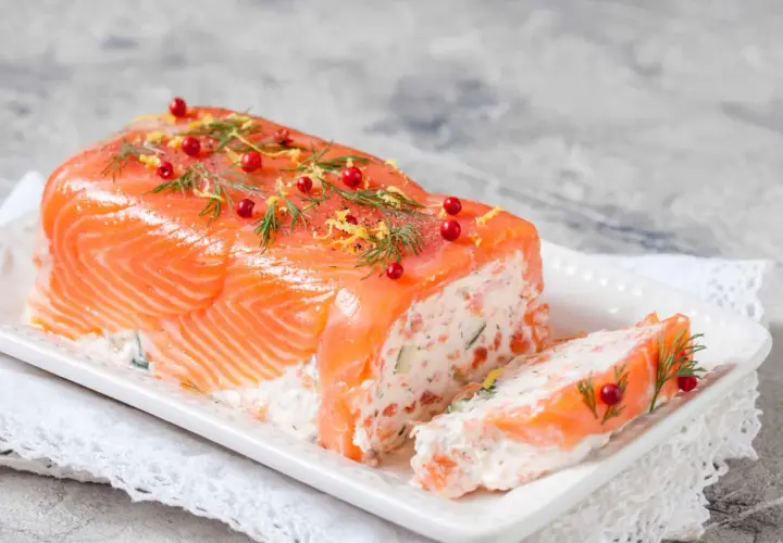 Une délicieuse terrine de saumon, garnie d'aneth, de baies roses et de zeste de citron, prête à être dégustée.
