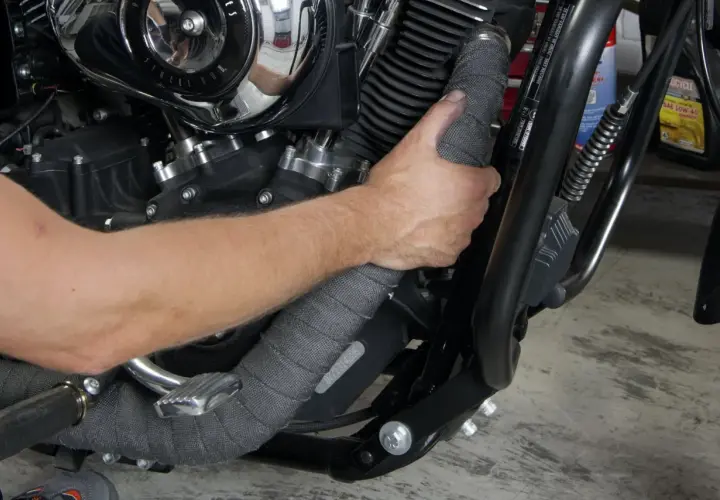 Mano che applica una fascia termica su un collettore di scarico di una moto.