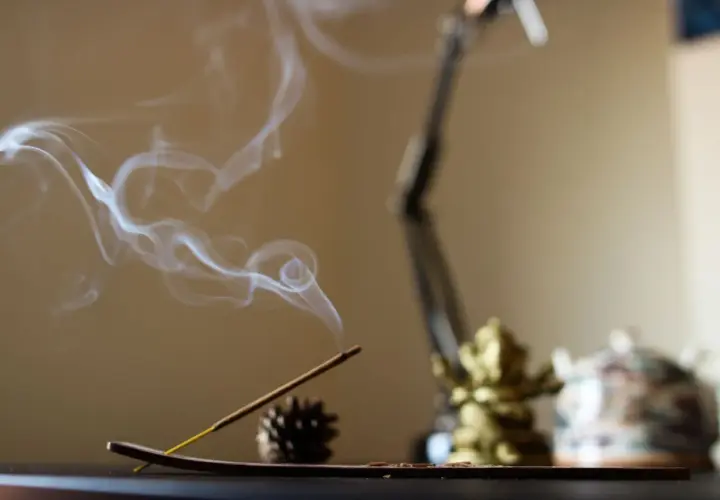 El humo del incienso se eleva en espirales blancas, creando un ambiente sereno junto a una figura dorada y una tetera decorada.