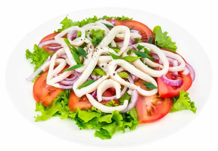 Deliziosa insalata di calamari con pomodori, cipolla rossa e lattuga fresca, condita con erbe aromatiche.