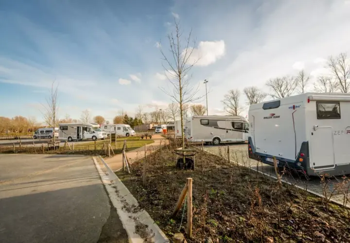 Vue d'une aire camping car Bruges avec plusieurs véhicules stationnés sous un ciel bleu.