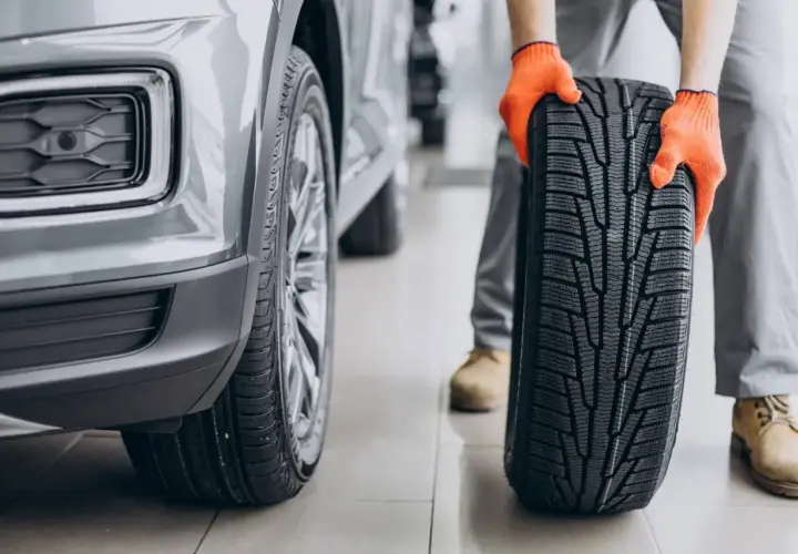 Mechanik w pomarańczowych rękawicach prezentuje nową oponę asymetryczną obok samochodu.